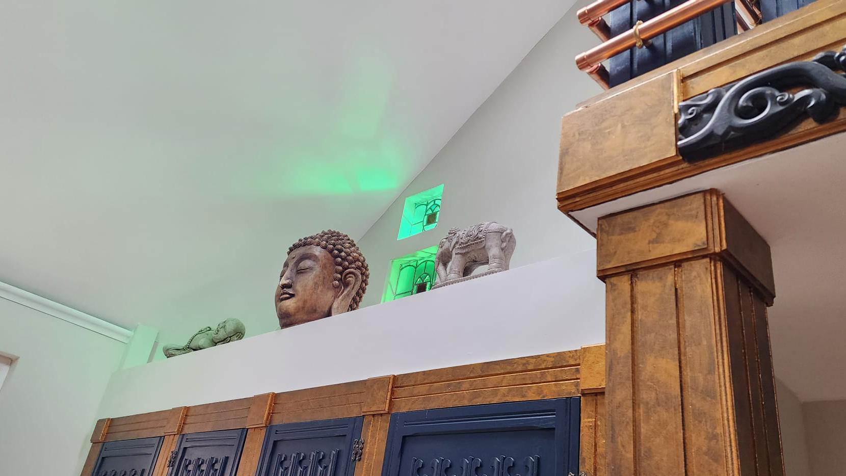 Large handmade wardrobe under an elevated platform with a budda head and other scultures with two small windows in the background