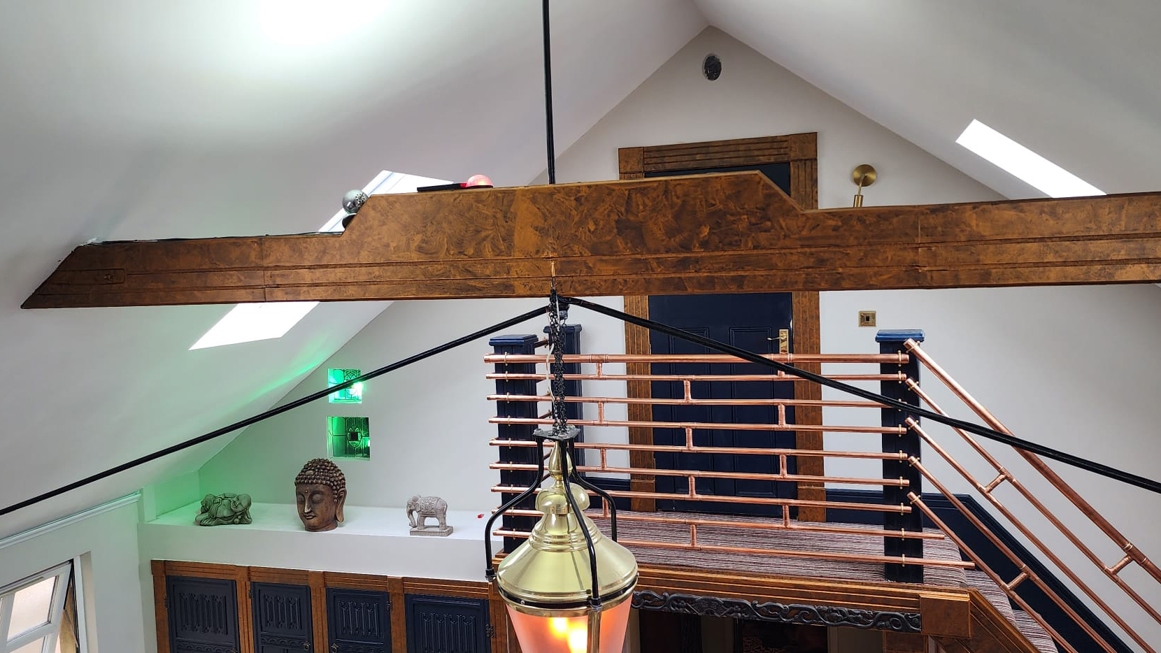 Oak beams located on two sloped celings with a view of the hanging pendant and staircase in the background leading to a room.