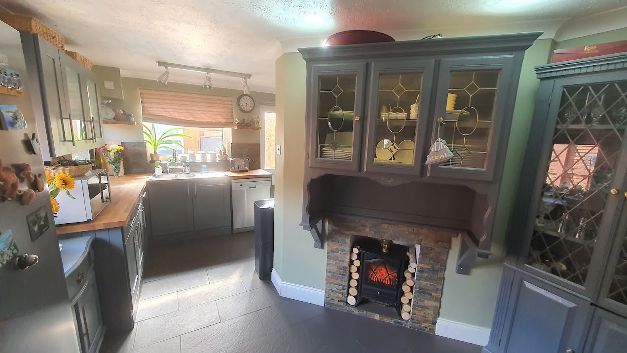 Dark grey matte cabinets within a kitchen with a fireplace and windows allowing sunlight to come through.