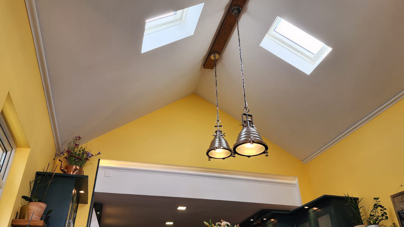 Two sloped celings with a piece of wood within the middle holding two hanging pendants.