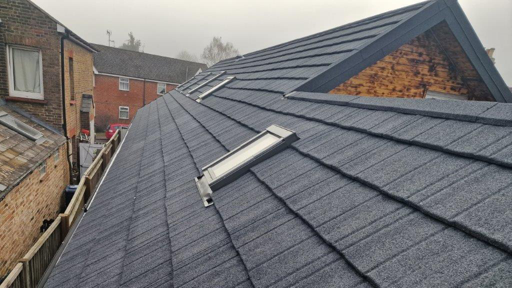 Newly installed grey tiled roof with skylight windows, viewed from the side of the house on a cloudy day.