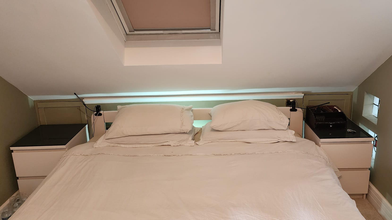 Bed with creme covers underneath a skylight in a sloped ceiling.