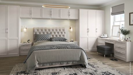 Grey bedroom with bed in the middle with a headboard, white cabinets around the bed.